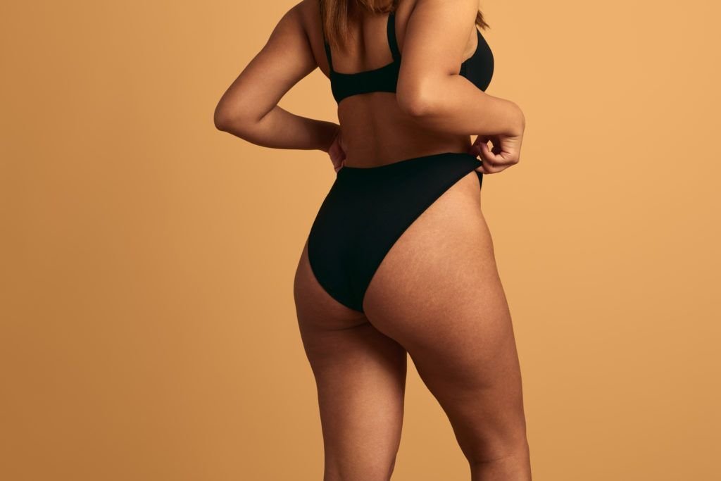 Back view of crop anonymous plus size woman in black lingerie demonstrating buttocks on brown background